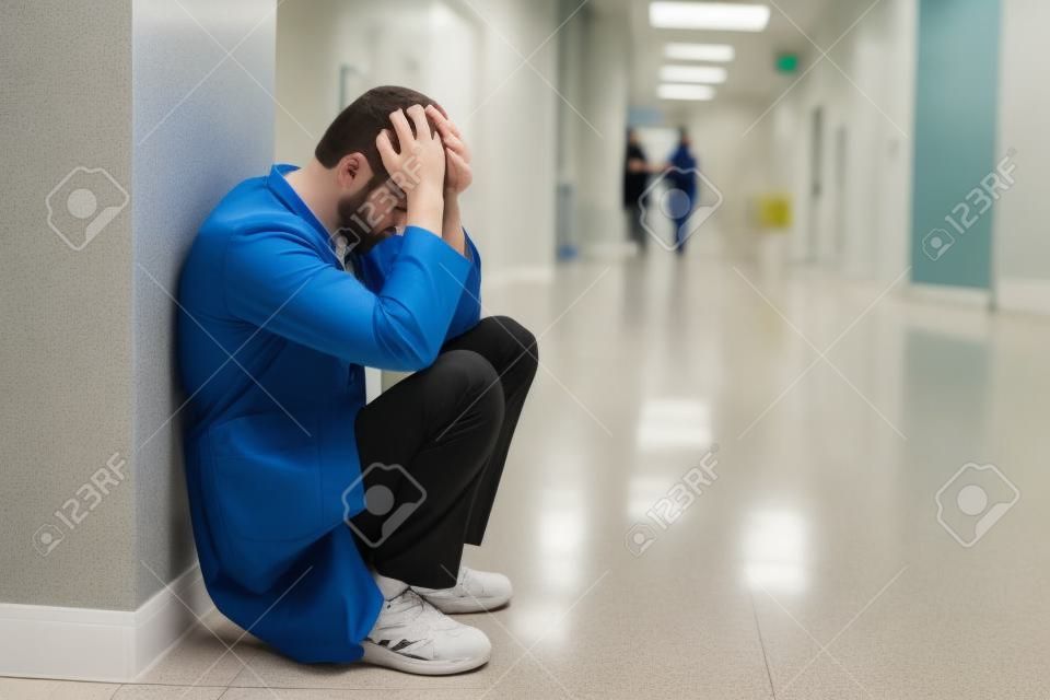 Upset young intern squatting in hospital corridor