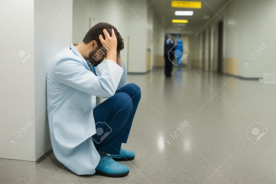 Upset young intern squatting in hospital corridor