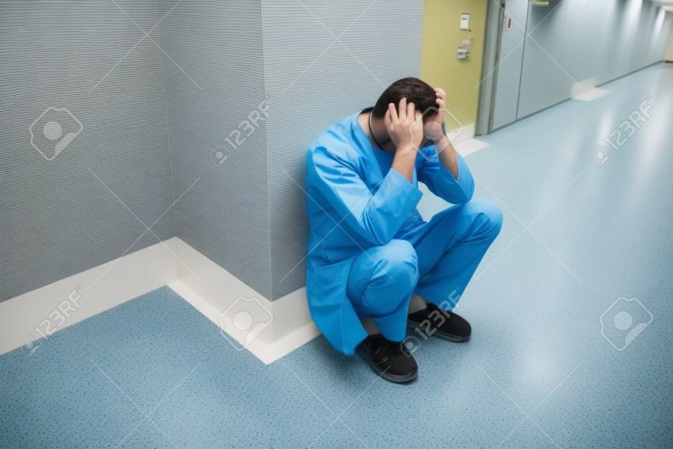 Sad young surgeon squatting in hospital corridor