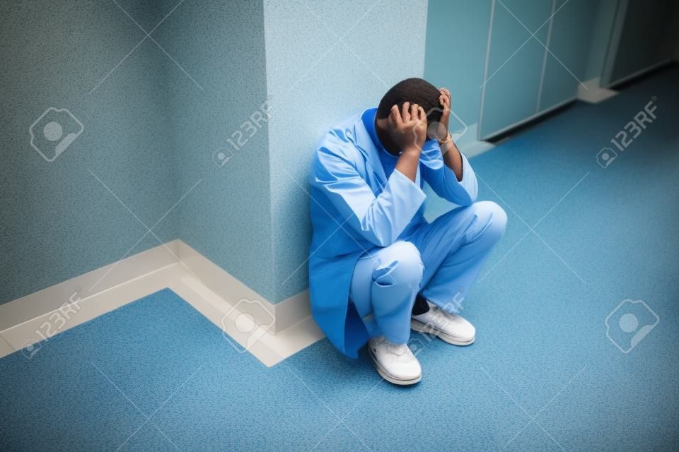 Sad young surgeon squatting in hospital corridor