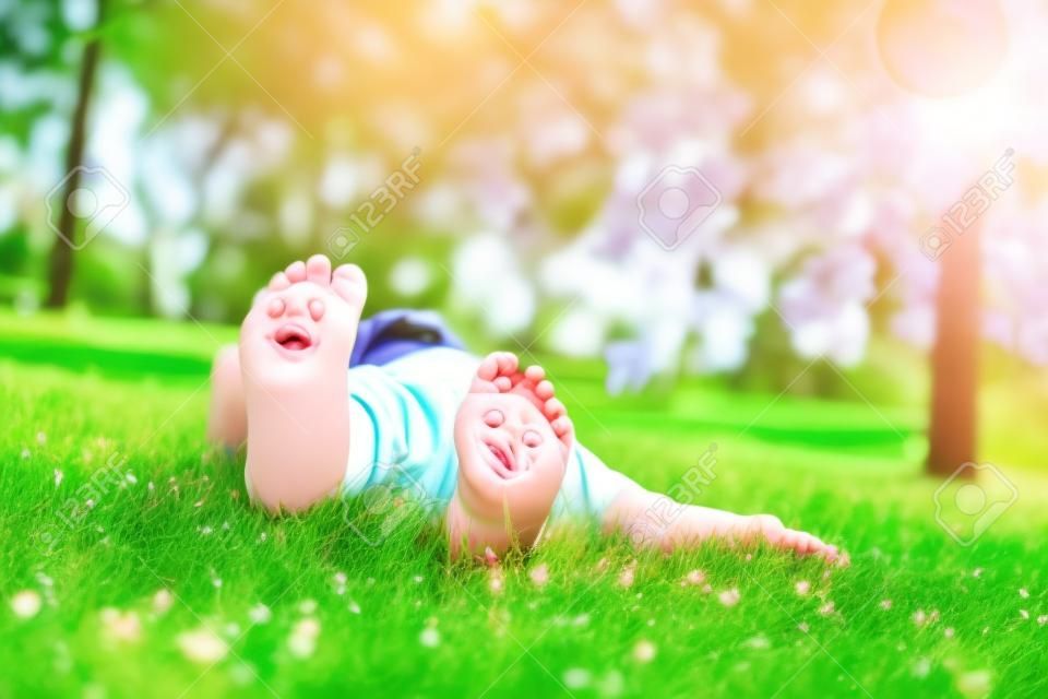 Dziecko leżące na zielonej trawie. Dziecko zabawy na świeżym powietrzu w parku wiosny. Natura.