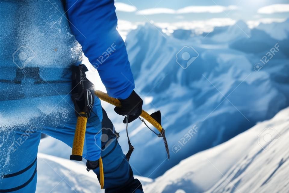 Close up A young guy climber holds in his hand an ice-ax standing on a summit high in the mountains. Extreme sport concept