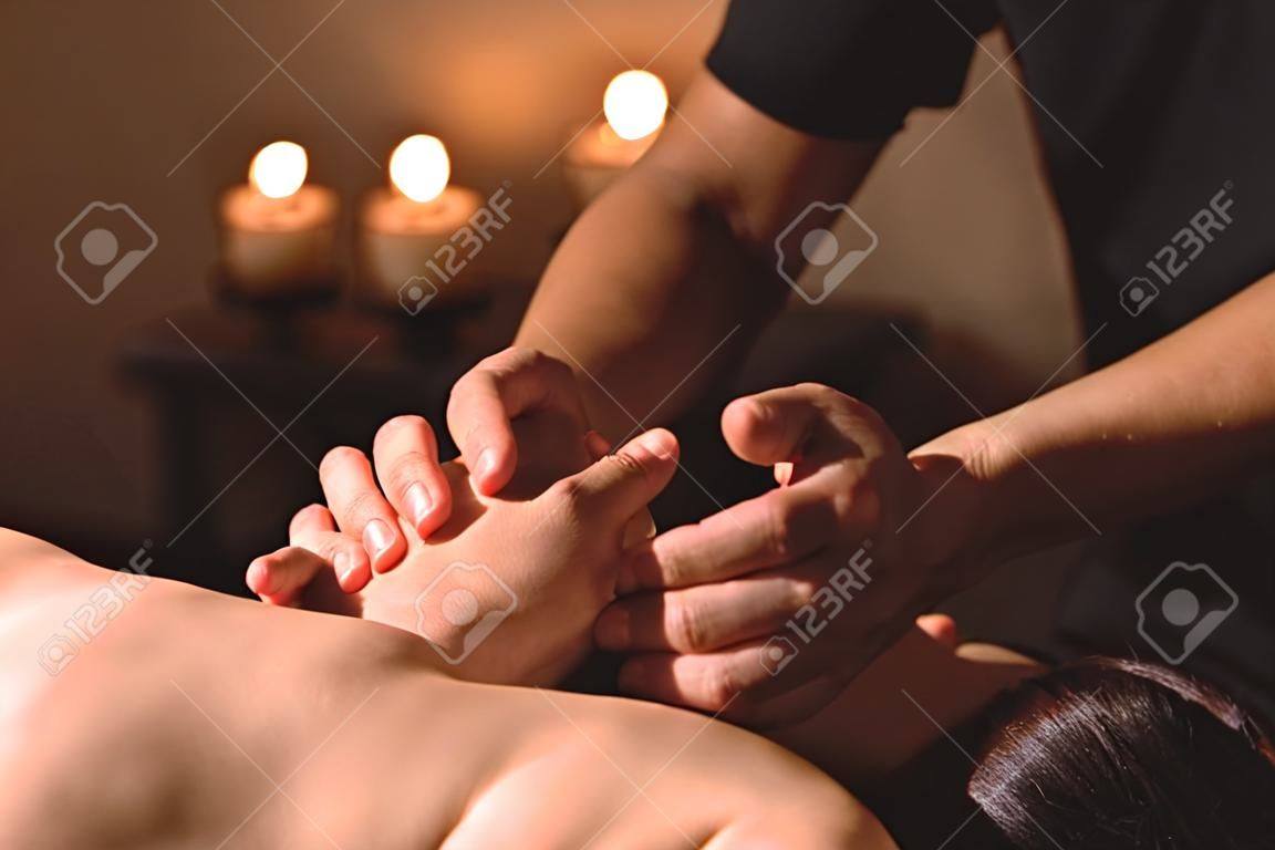 Mens hands make a therapeutic neck massage for a girl lying on a massage couch in a massage spa with dark lighting. Close-up. Dark Key