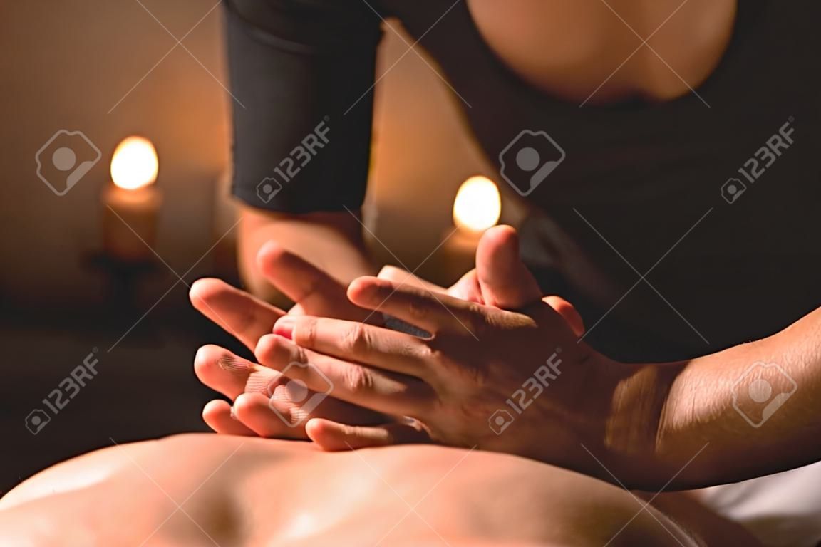 Männerhände machen eine therapeutische Nackenmassage für ein Mädchen, das auf einer Massageliege in einem Massage-Spa mit dunkler Beleuchtung liegt. Nahansicht. Dunkler Schlüssel