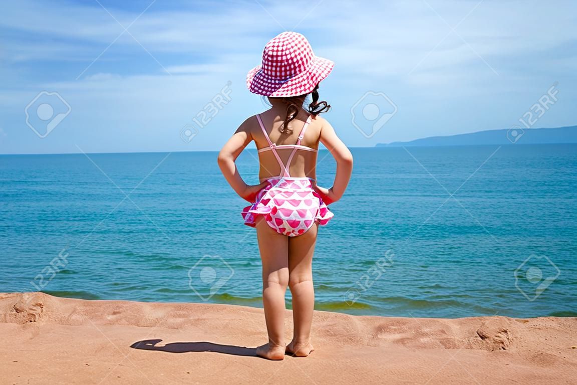 Bambina in un vestito di nuoto guarda il mare