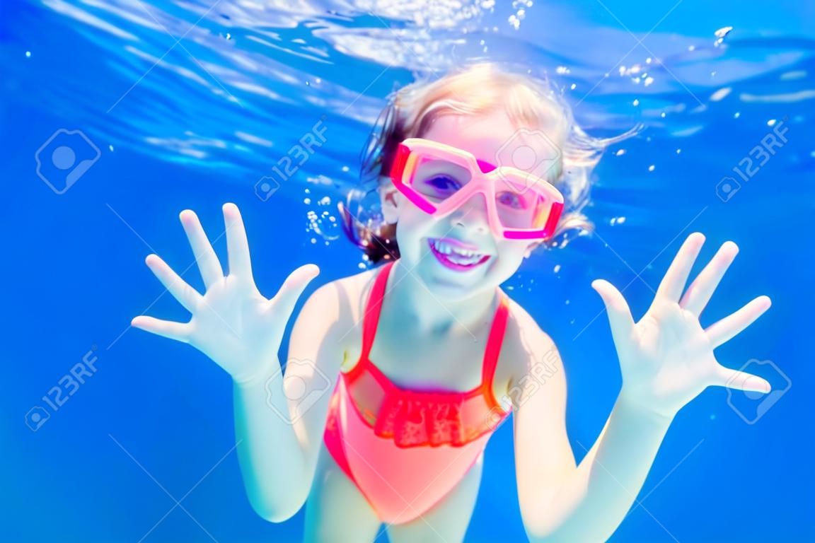 Cheerful little girl playing under  water in pool. Underwater photo.