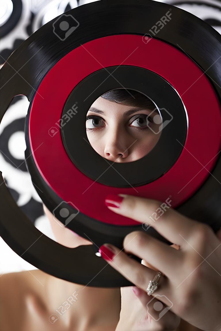 young woman looking through the hole of a small dusty record with a red label