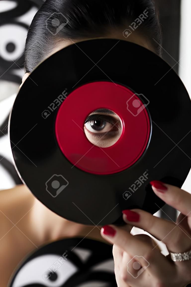 young woman looking through the hole of a small dusty record with a red label