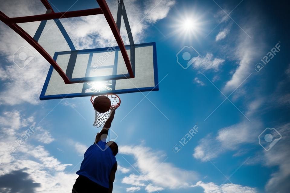 silihouette basketball player from bottom view with slam dunk to catch ball on blue sky. outdoor sport on day light