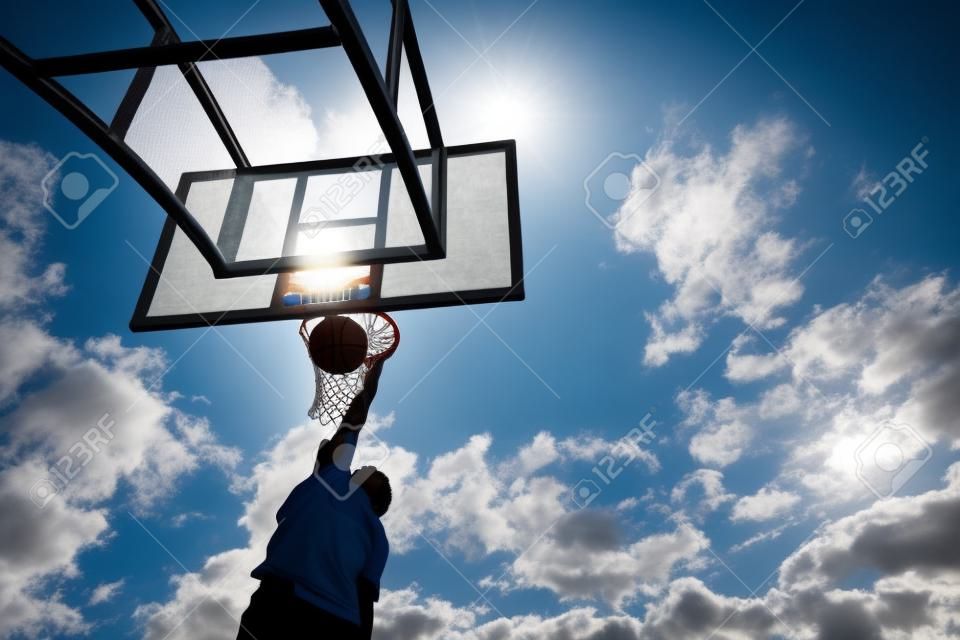 silihouette basketball player from bottom view with slam dunk to catch ball on blue sky. outdoor sport on day light
