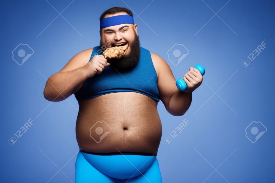 L'uomo più divertente mangia la coscia di pollo e fa esercizi con il manubrio su sfondo blu