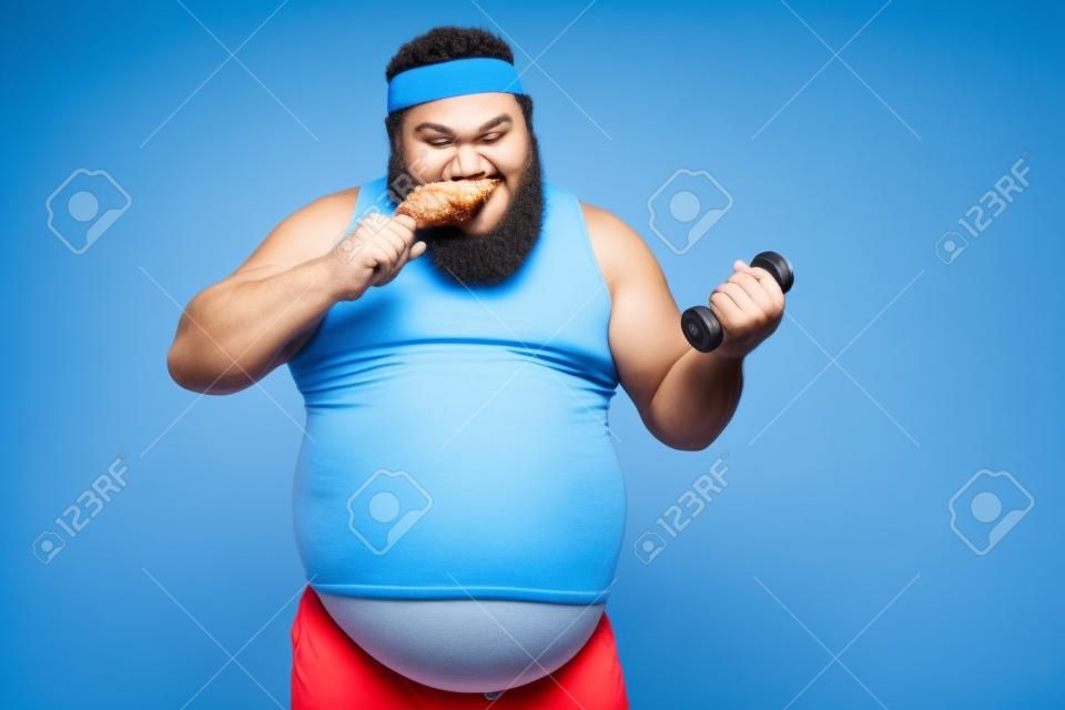 L'uomo più divertente mangia la coscia di pollo e fa esercizi con il manubrio su sfondo blu