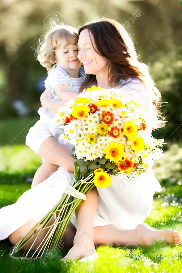 Happy child and woman with bouquet of spring flowers sitting on green grass. Mother`s day concept