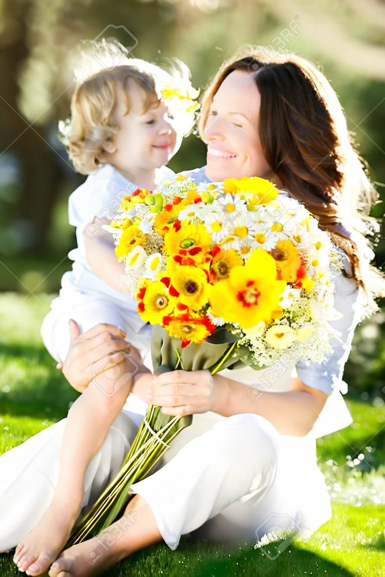 Glückliches Kind und Frau mit Blumenstrauß der Frühlingsblumen sitzen auf grünem Gras. Mother `s day concept