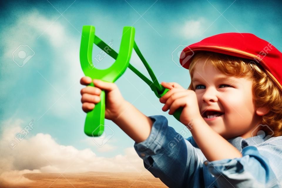Kid holding slingshot in hands against summer sky background. Retro style