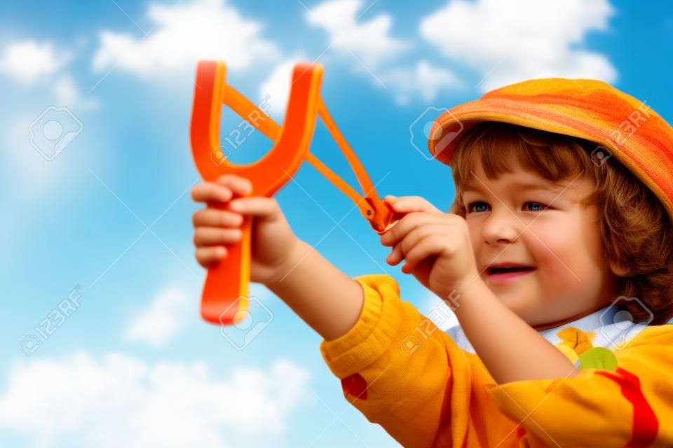 Kind mit Steinschleuder in der Hand gegen die Sommer-Himmel Hintergrund. Retro-Stil