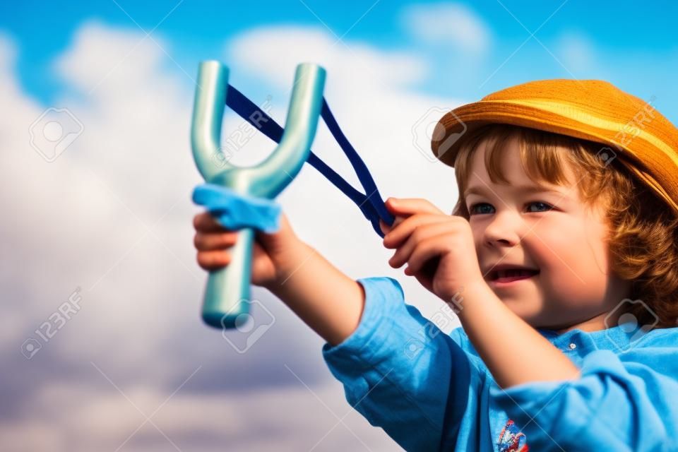 Малыш держит рогатку в руках против летом фоне неба. Ретро стиль