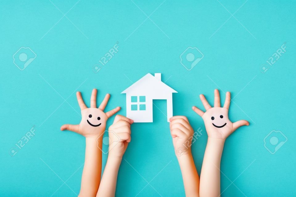 Glückliche Kinder mit Smiley auf Händen halten Papier grünes Haus gegen blauen Sommerhimmel Hintergrund