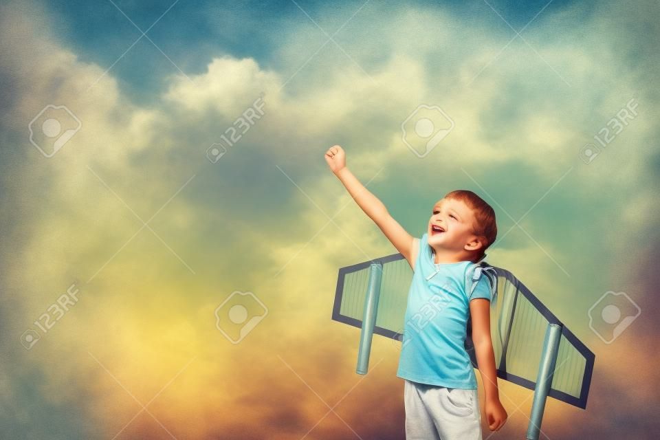 Criança feliz brincando com asas de brinquedo contra o fundo do céu de verão.