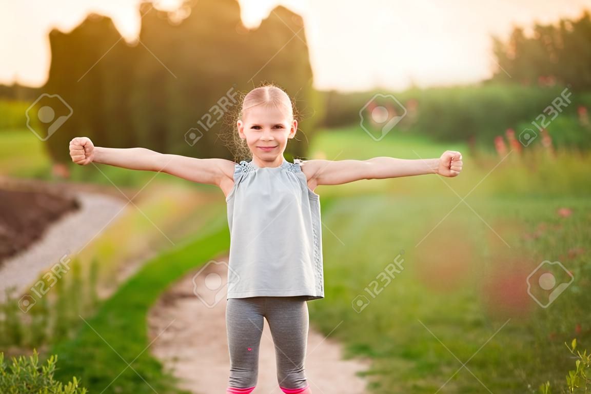 Bambino ragazza carina mostra bicipite gesto di potenza e forza all'aperto. Sentiti così potente. Concetto di regole per ragazze. Forte e potente.