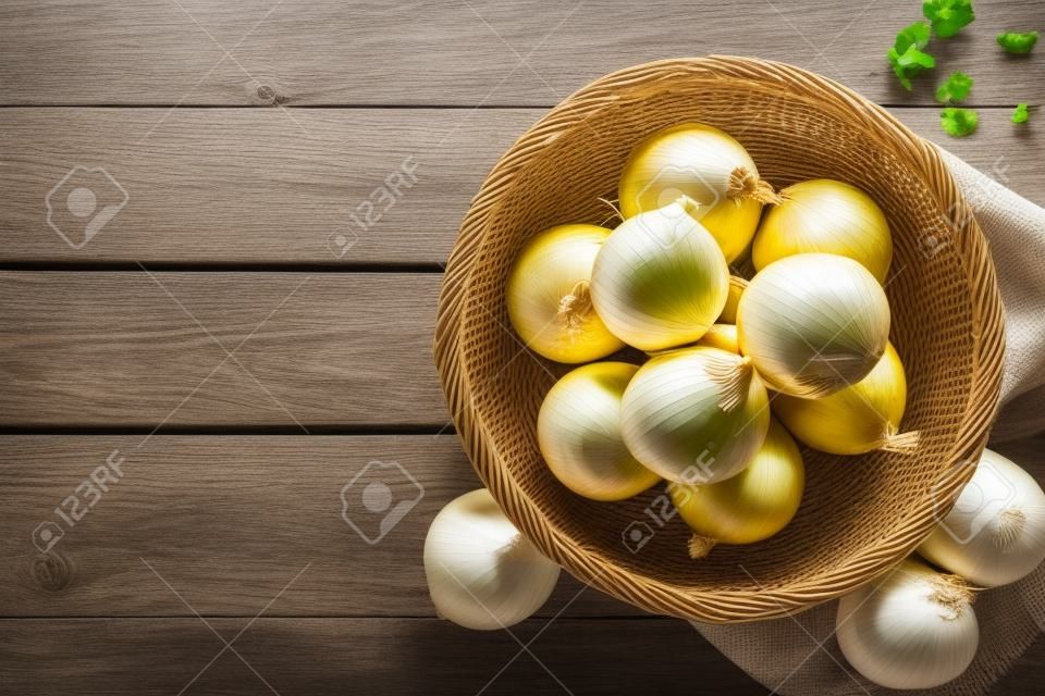 Fresh onion in basket on wooden table, top view