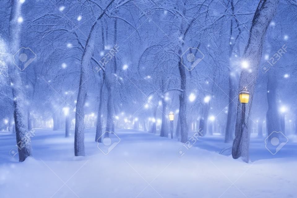 Winter night park with lanterns, pavement and trees covered with snow in heavy snowfall.