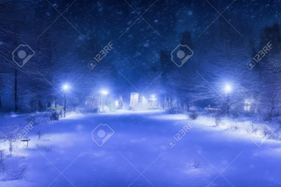 Blured photo of a winter night park with lanterns and Christmas decorations in heavy snowfall.