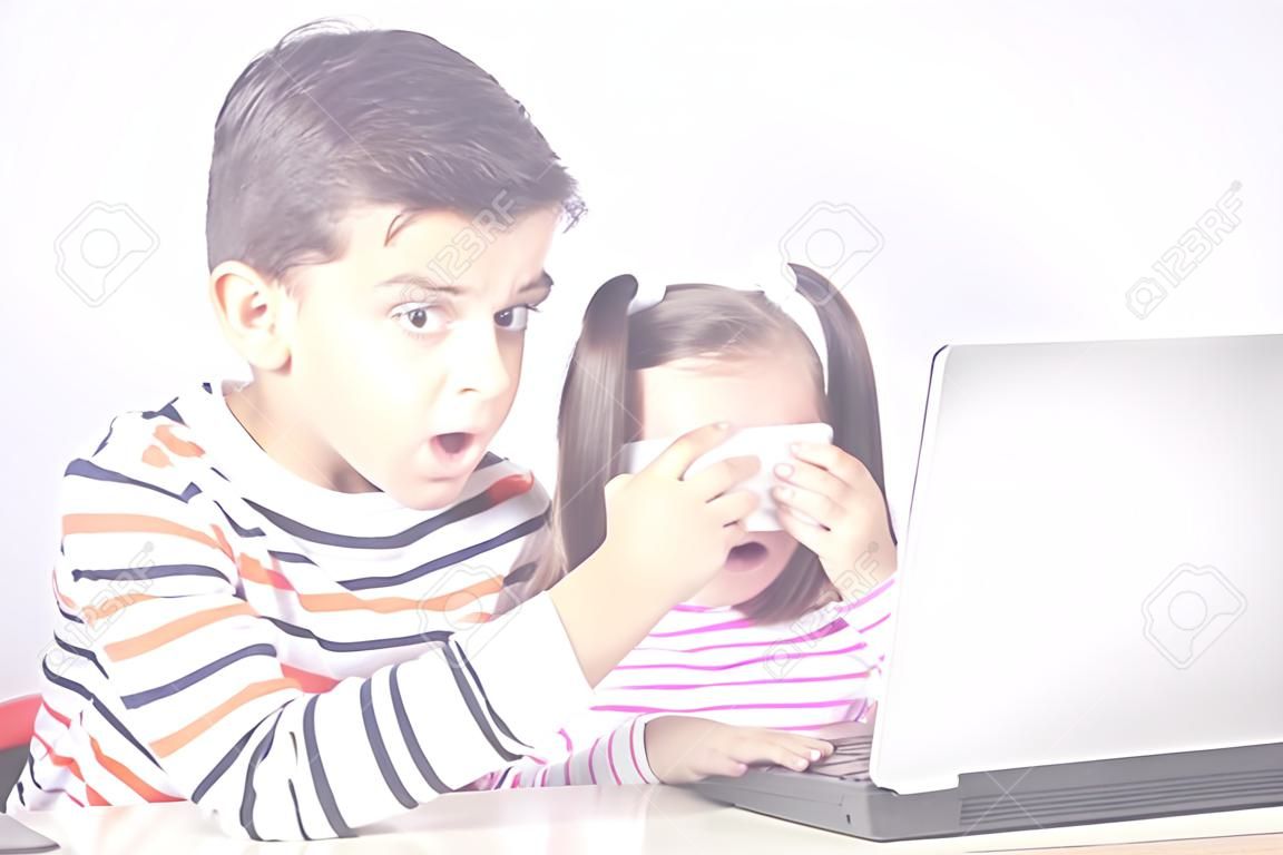 Der kleine Junge schützt seine Schwester davor, unangemessene Inhalte zu sehen, während sie einen Computer benutzt. Konzept der Internetsicherheit für Kinder
