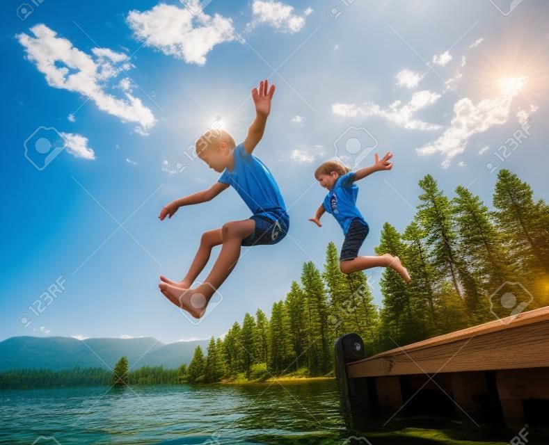 Crianças pulando da doca em um belo lago de montanha. Divertindo-se em umas férias de verão no lago com os amigos