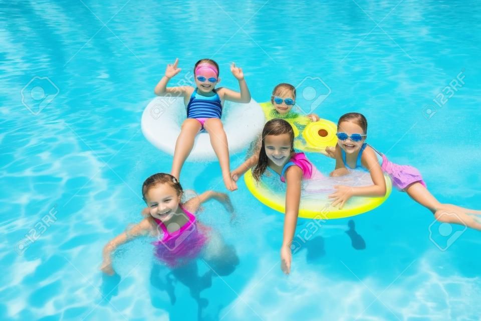 Group of cute little girls playing at an outdoors swimming pool on a warm summer day. Floating in the pool together and having fun