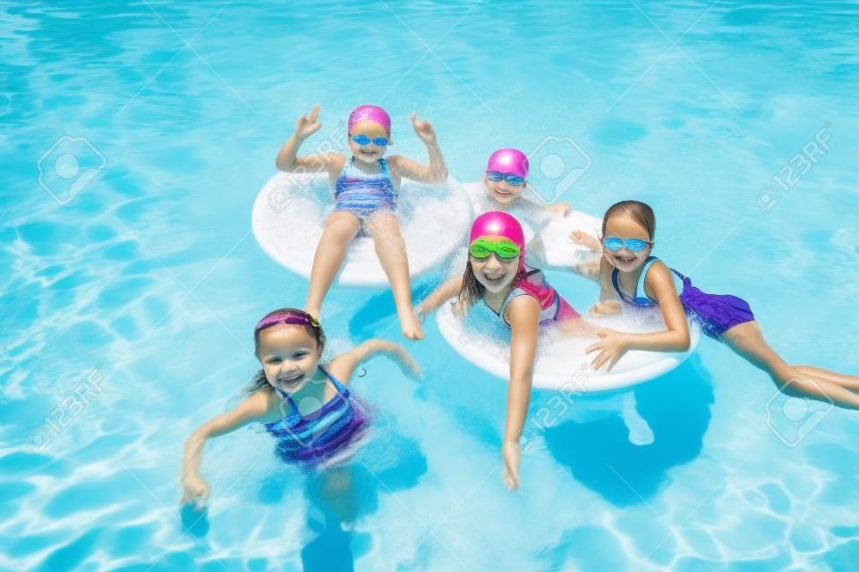 Group of cute little girls playing at an outdoors swimming pool on a warm summer day. Floating in the pool together and having fun