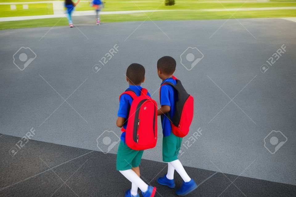 Two diverse school kids walking and talking together on the way to school. Back to school photo of diverse school children wearing backpacks in the school yard
