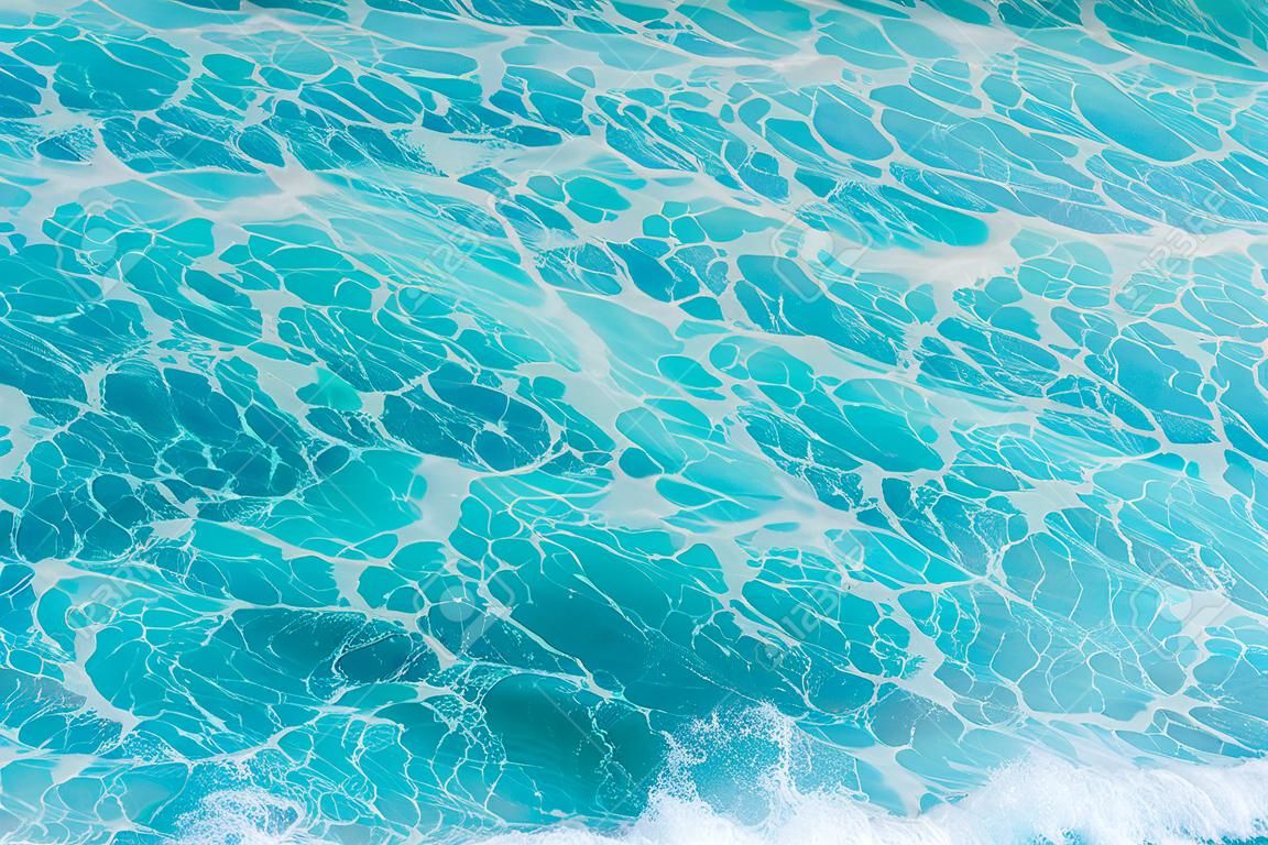 The azure surface of the ocean. Waves break at the shore. Texture of the water surface near the shore above the coral reef. Aerial photography of water. Azure sea natural background.