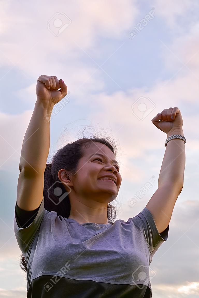 A single female figure with a gesture of congratulating success with a bright sky in the background