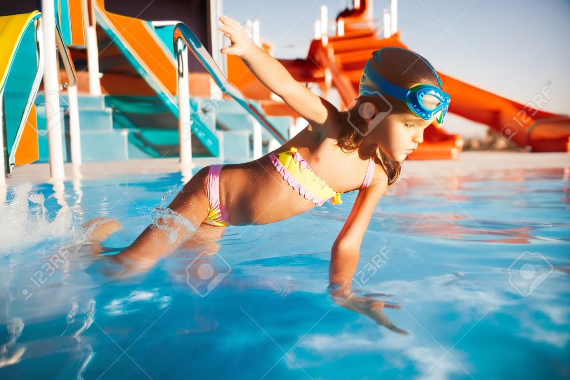 A cheerful girl in blue goggles for swimming whirls in a pool with clear clear water with her hands in the water
