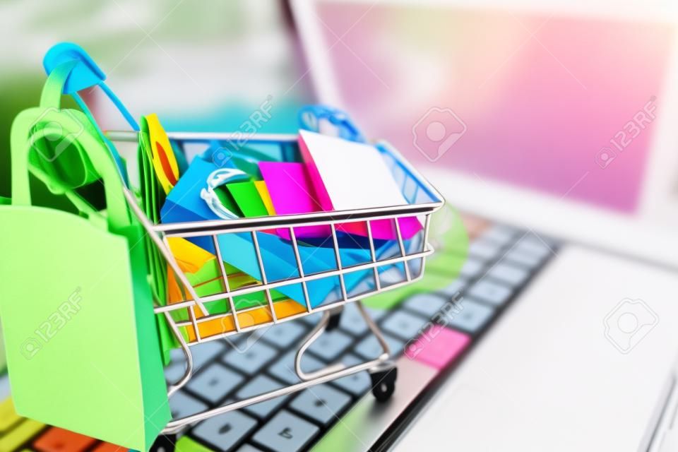 Concepto en línea de compras, bolsa de papel de colores en carro en la computadora portátil.