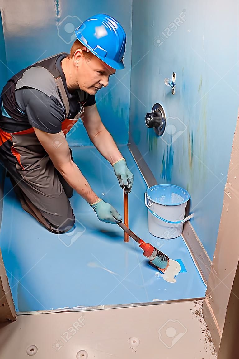 De werknemer brengt waterdichte verf op de vloer in de badkamer.