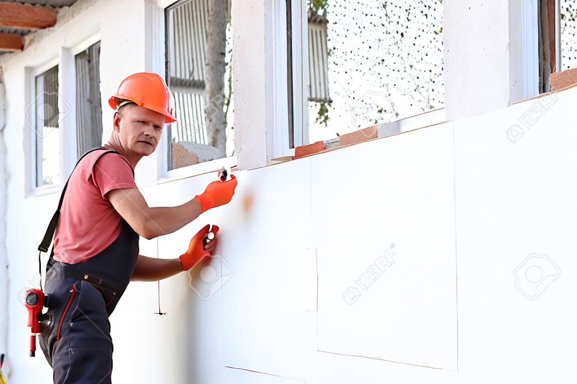 Aislamiento de la casa con poliespuma. El trabajador está comprobando con el nivel de construcción la precisión de la instalación de tablero de poliestireno en la fachada.