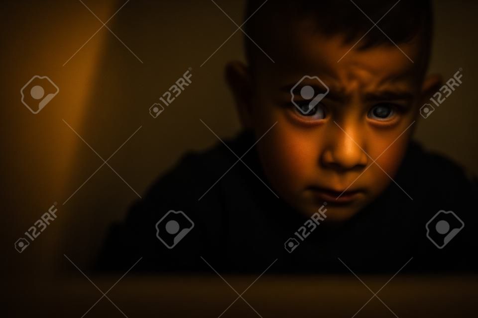 Niño sentado en la esquina de la habitación en la oscuridad con miedo y desesperanza