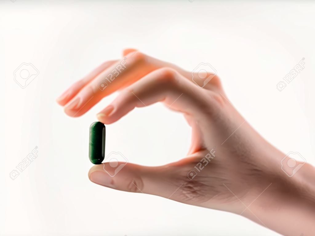 Hand holding a green capsule pill on white background