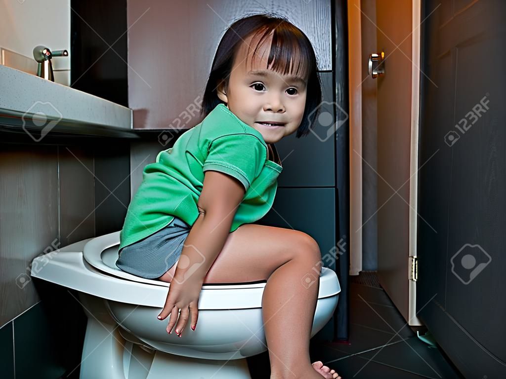 Adorable Asian child girl sitting on toilet bowl at home in the morning. Health care concept.