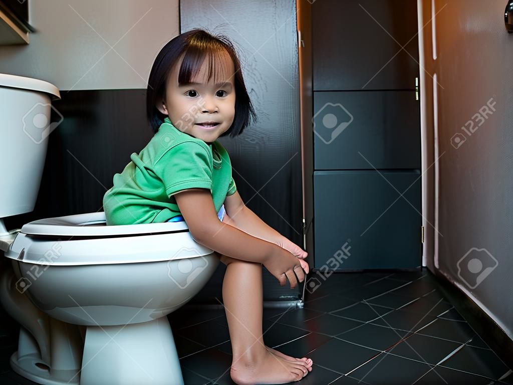 Entzückendes asiatisches Kindermädchen, das morgens zu Hause auf Toilettenschüssel sitzt. Gesundheitskonzept.