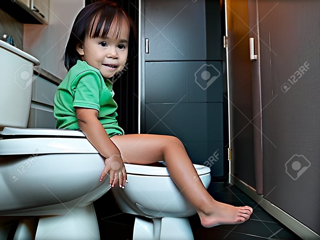 Adorable Asian child girl sitting on toilet bowl at home in the morning. Health care concept.