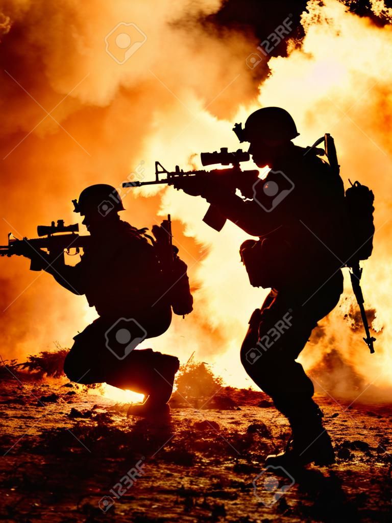 Negro siluetas de par de soldados en el fuego de humo quemando en movimiento en la operación de batalla. Luz trasera