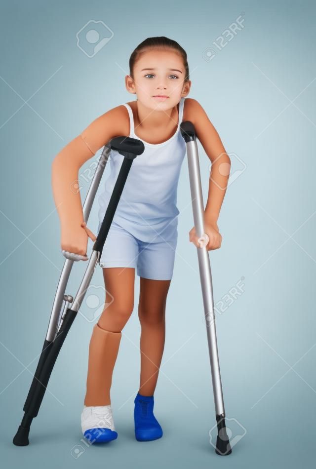 Een jong meisje worstelt om te lopen met krukken na verwondingen aan haar arm en been.
