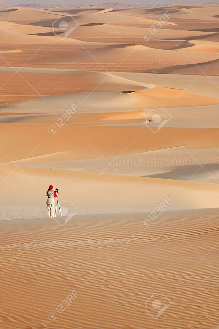 A woman photographing sand dunes in the Rub al Khali or Empty Quarter. Straddling Oman, Saudi Arabia, the UAE and Yemen, this is the largest sand desert in the world.