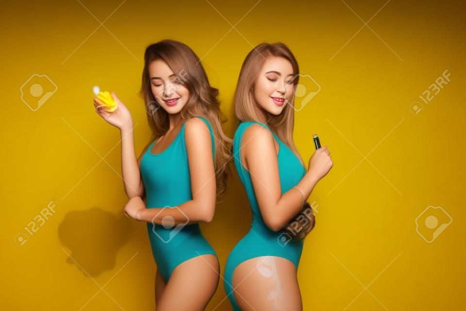 Zwei junge Frauen in Bodys, die im Studio Dampf auf gelbem Hintergrund pusten.