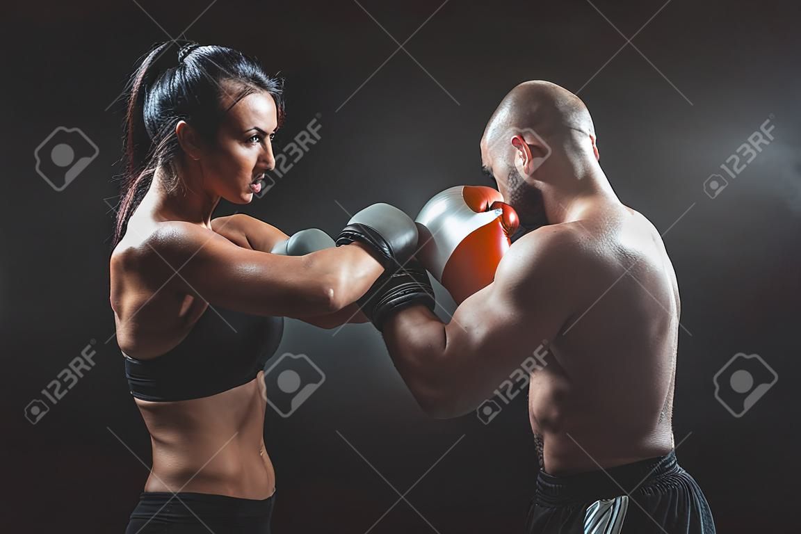 Shirtless Woman trainen met trainer bij boksen en zelfverdediging les, studio, donkere achtergrond. Vrouw en man vechten.