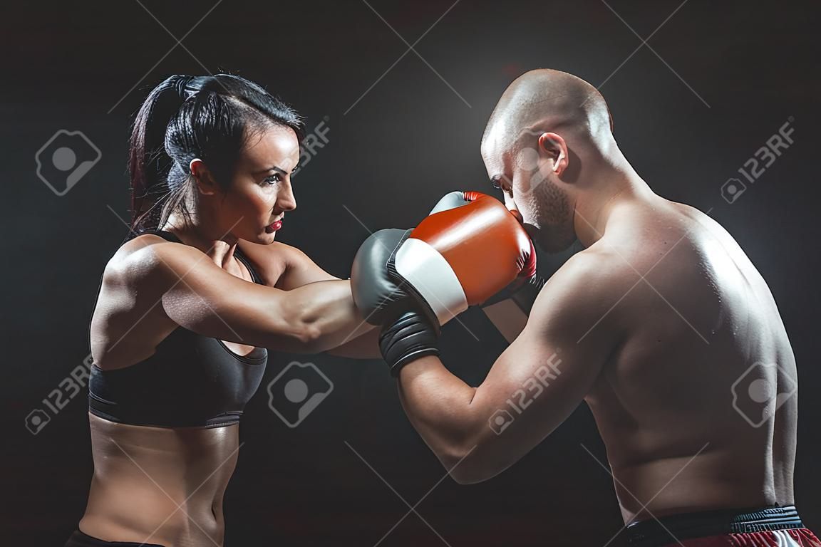 Shirtless Woman trainen met trainer bij boksen en zelfverdediging les, studio, donkere achtergrond. Vrouw en man vechten.