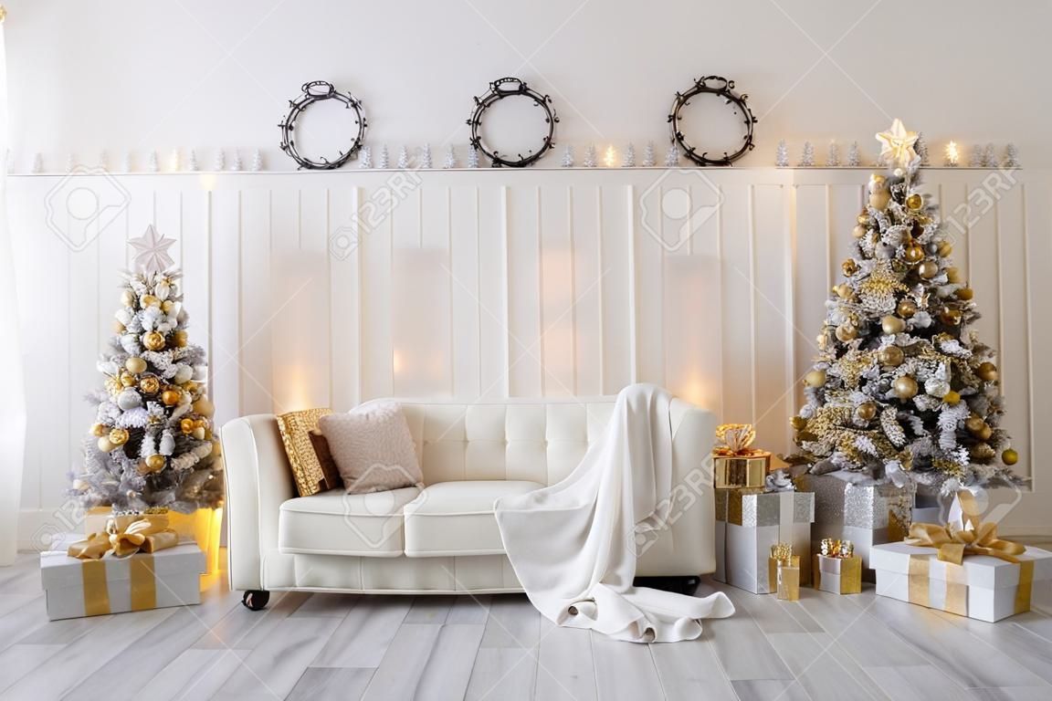Weißes Wohnzimmer mit Neujahrsbäumen, Geschenkboxen und modernem Sofa. goldene Farbe